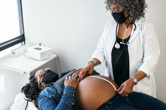 Black doctor measures abdomen of pregnant woman, wearing mask during pandemic