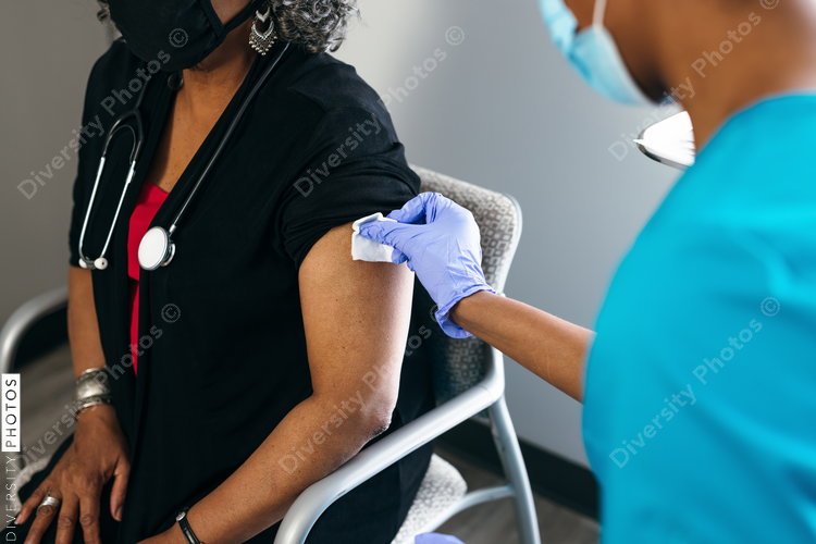 Senior female doctor gets vaccine, from black nurse