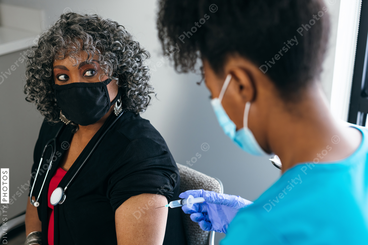 Senior female doctor gets vaccine, from black nurse