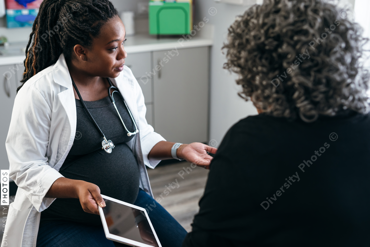 Black pregnant doctor explains lab results to senior patients using digital tablet 