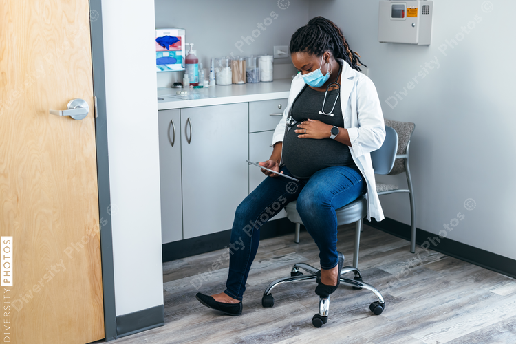 Black pregnant doctor reviewing medical records on tablet