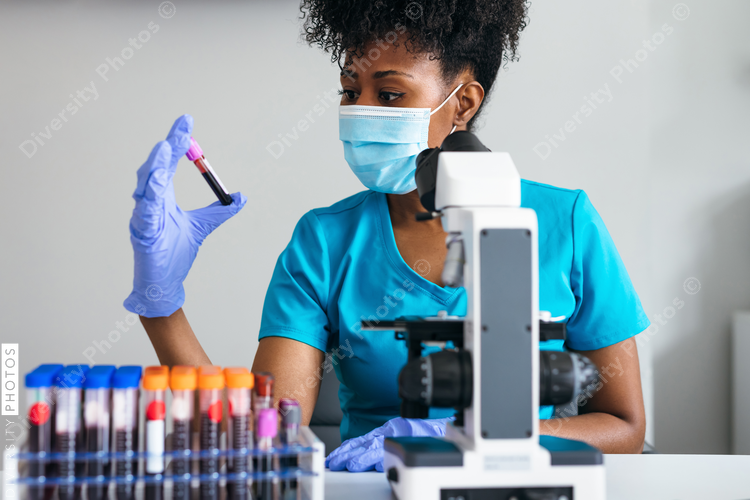 Black medical professional in a mask looks at blood sample label