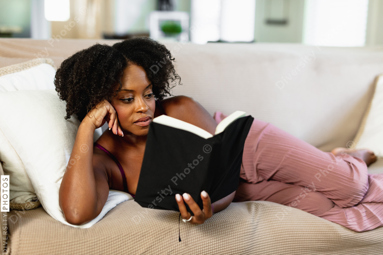 African American woman in pajamas reading book at home, comfort 