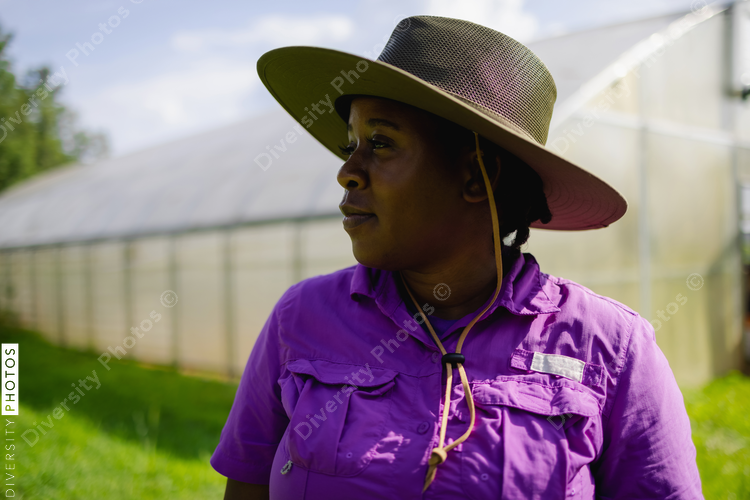 Portrait of African American female farmer standing in field in front of greenhouse at organic¬†farm