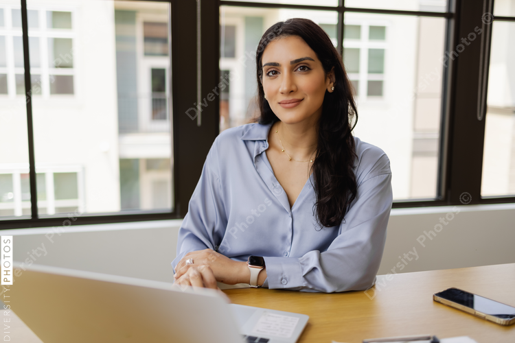 Portrait of young businesswoman with laptop in office, Middle Eastern, tech company