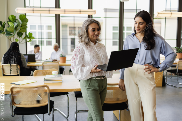 Professional businesswomen using laptop, mentoring colleague, Middle Eastern and Chinese