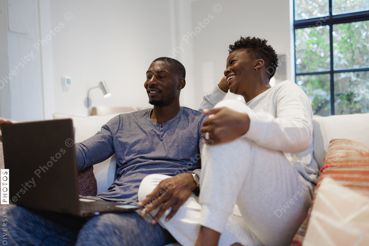 Smiling couple sitting on sofa and using laptop