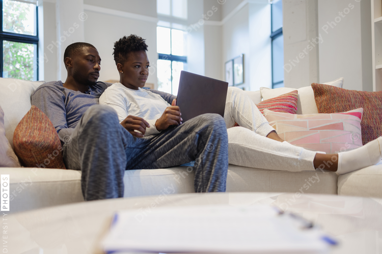 Black Couple sitting on sofa and using laptop