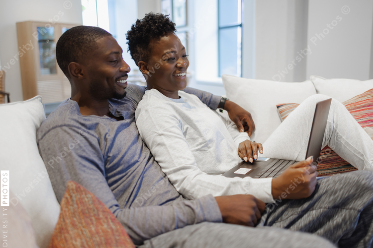 Smiling couple sitting on sofa and using laptop