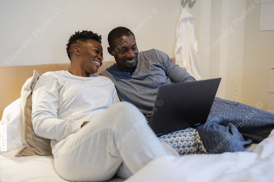 African American Smiling couple lying in bed and using laptop
