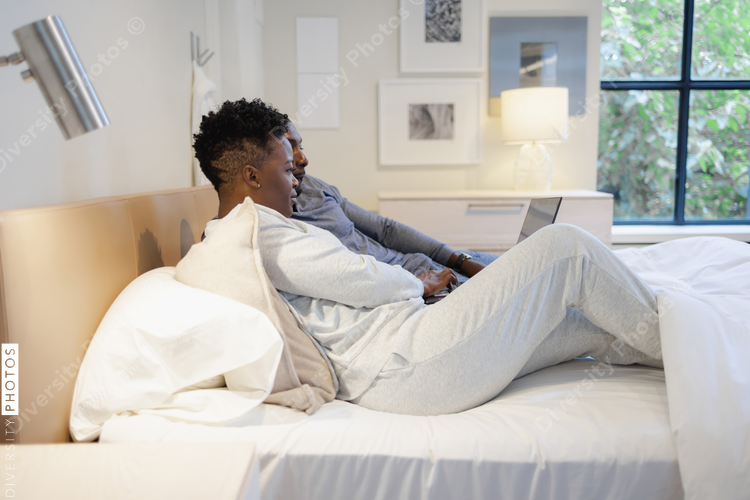 Black Couple lying in bed and using laptop