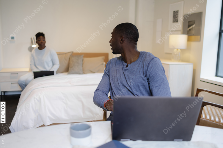 Couple using laptops in bedroom