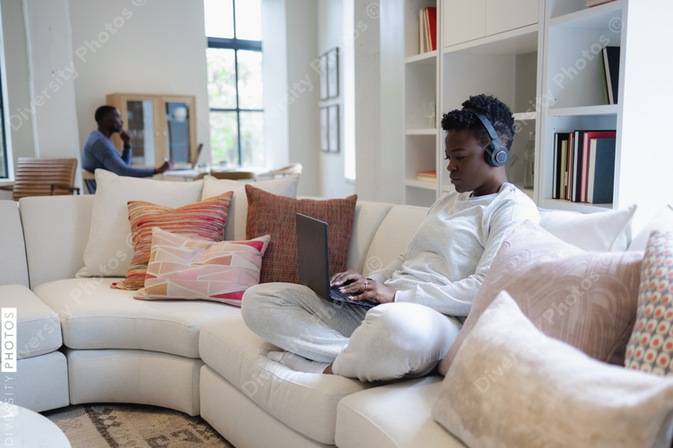 Black Woman in headphones sitting on sofa and using laptop