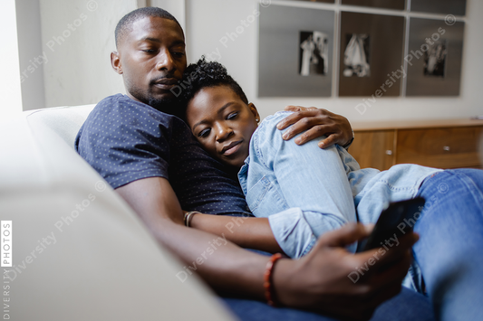 Black Couple cuddles lying on sofa and using smart phone