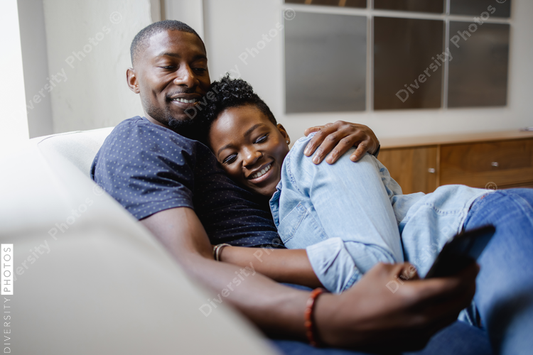 Smiling couple lying on sofa and using smart phone