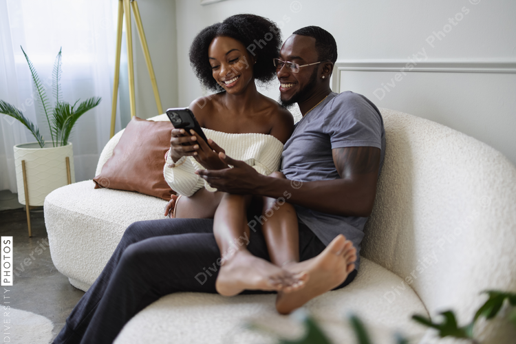 Smiling couple sitting on sofa and using smart phone