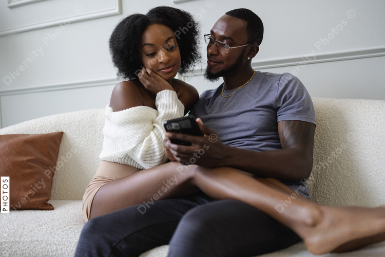 Smiling couple sitting on sofa and using smart phone