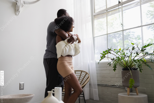 Black Couple hugging in living room and looking through window