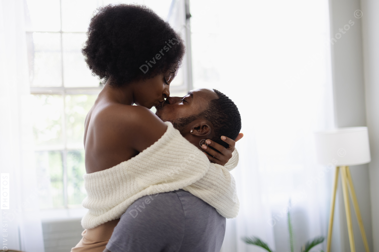 Young Black couple kissing in living room, anniversary 