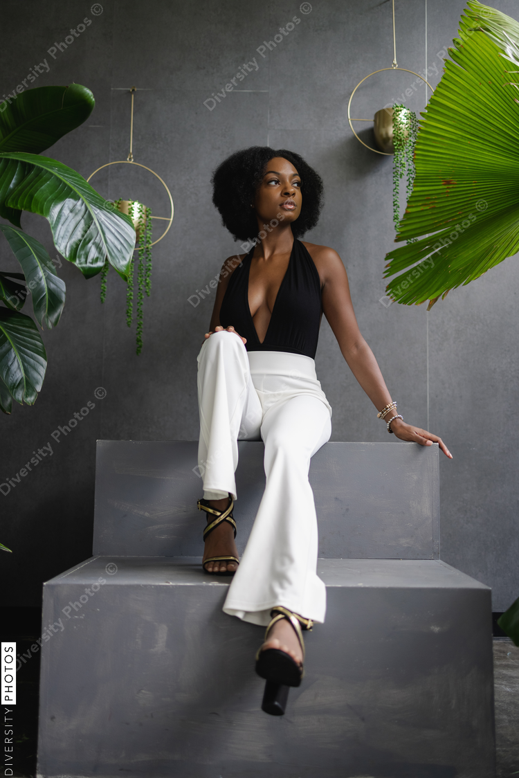 Elegant young Black woman sitting on steps among plants