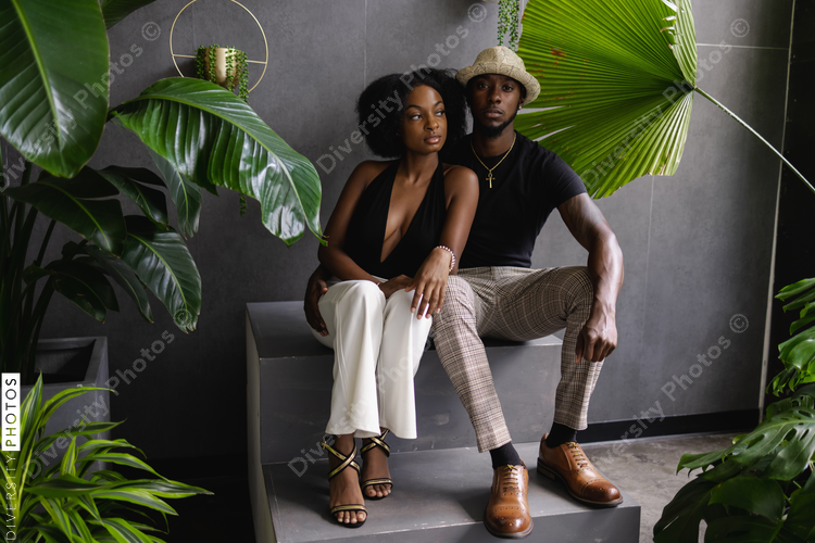 Fashionable Black young couple sitting on steps among plants