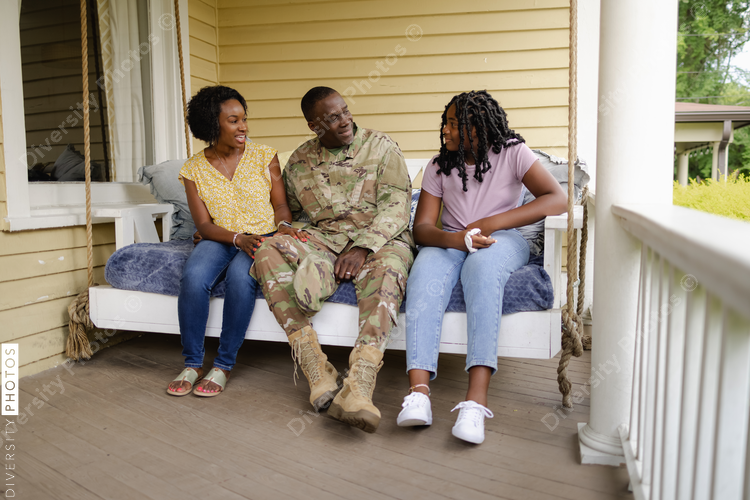 Military dad talks with wife and daughter on front porch swing, African American
