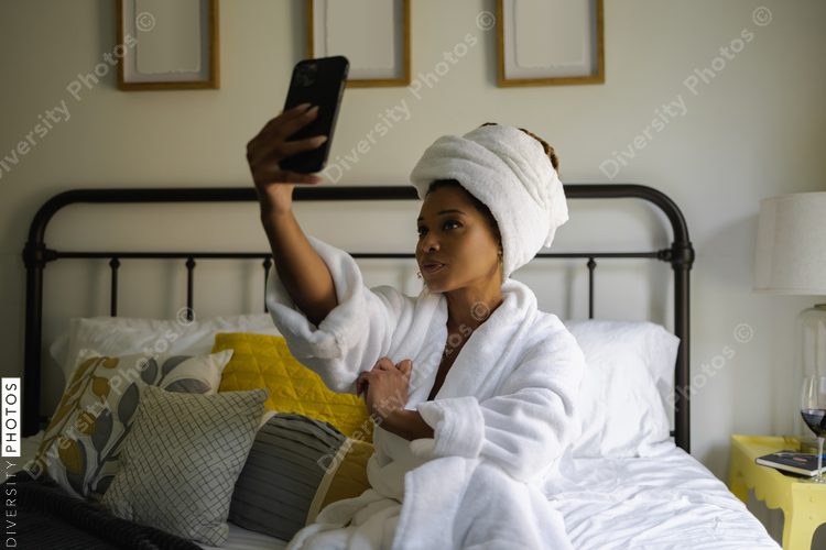 Woman in bathrobe taking selfie on bed