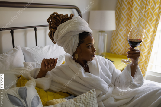 African American Woman in bathrobe relaxing in bed with glass of wine
