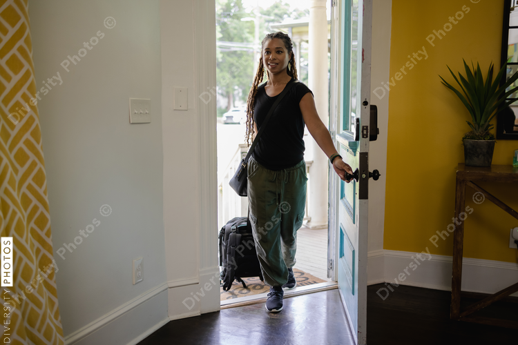 African American Woman with luggage entering house, vacation, urban
