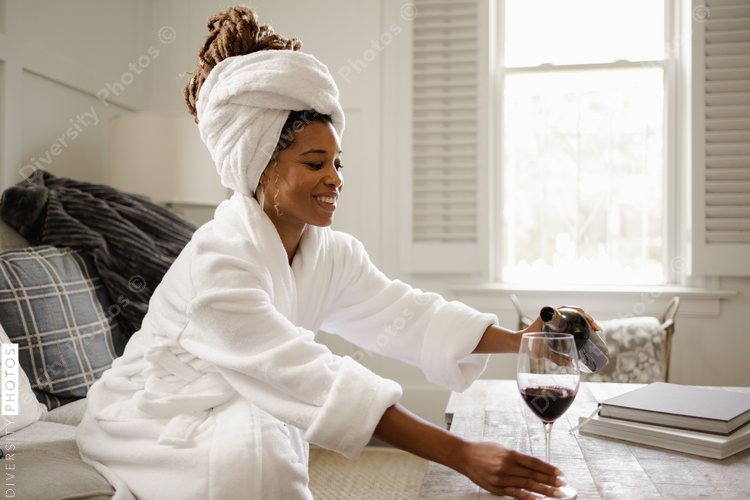 Black Woman in bathrobe sitting on sofa, pouring glass of wine
