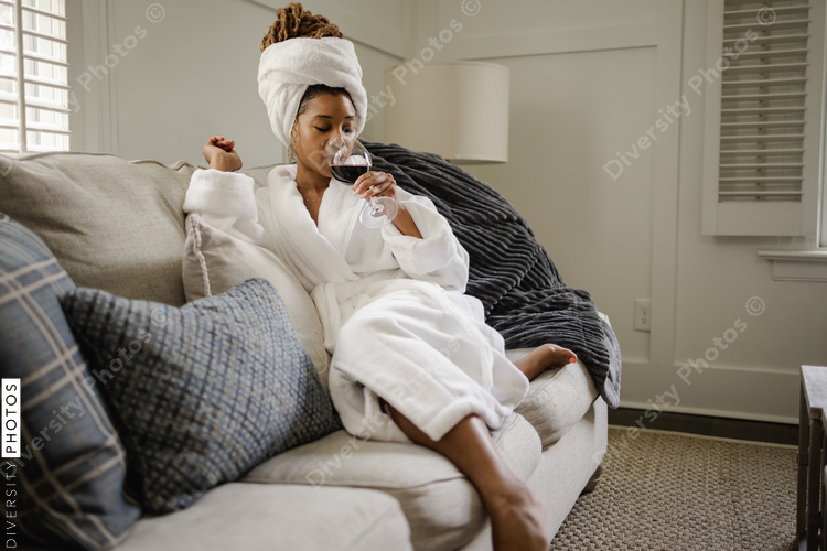African American Woman in bathrobe sitting on sofa, drinking wine