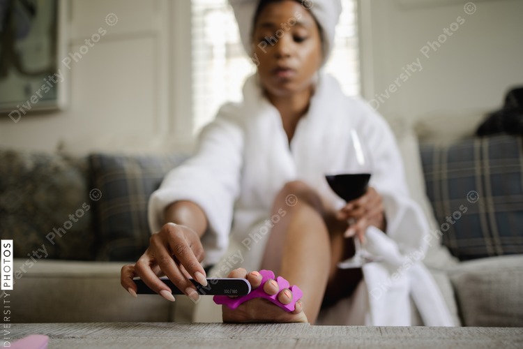 Woman in bathrobe drinking wine while doing pedicure