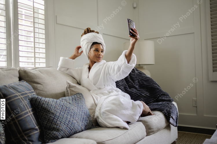 Woman in bathrobe taking selfie on sofa