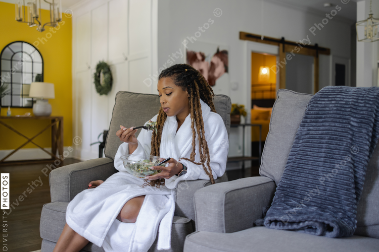 Woman in bathrobe eating salad in living room