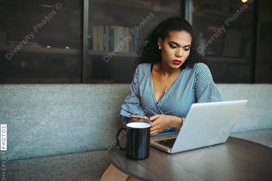 Young businesswoman using smartphone while looking at laptop