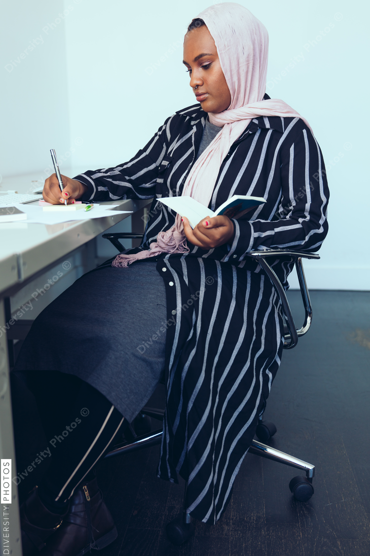 Businesswoman writing in book while sitting in office