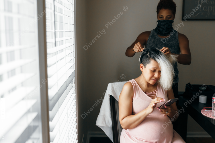 Pregnant black woman having hair done and self-care by hairdresser in mask during Covid-19