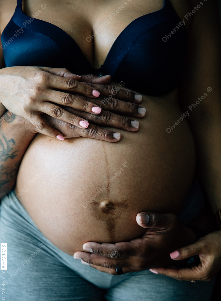 Black couples hands around stomach in third trimester pregnancy