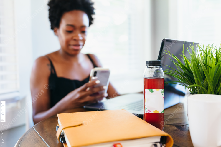 Woman working remotely from home on smartphone with wellness drink