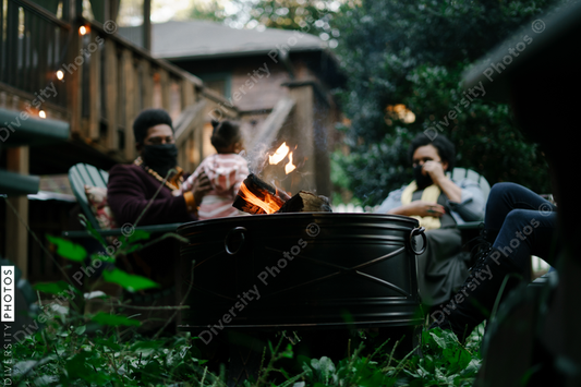 Black friends sitting around firepit safely wearing mask in backyard