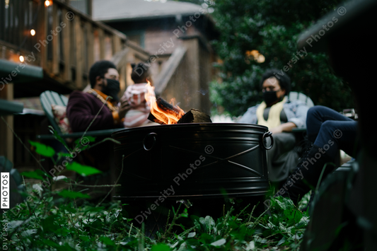 Black friends sitting around firepit safely wearing mask in backyard