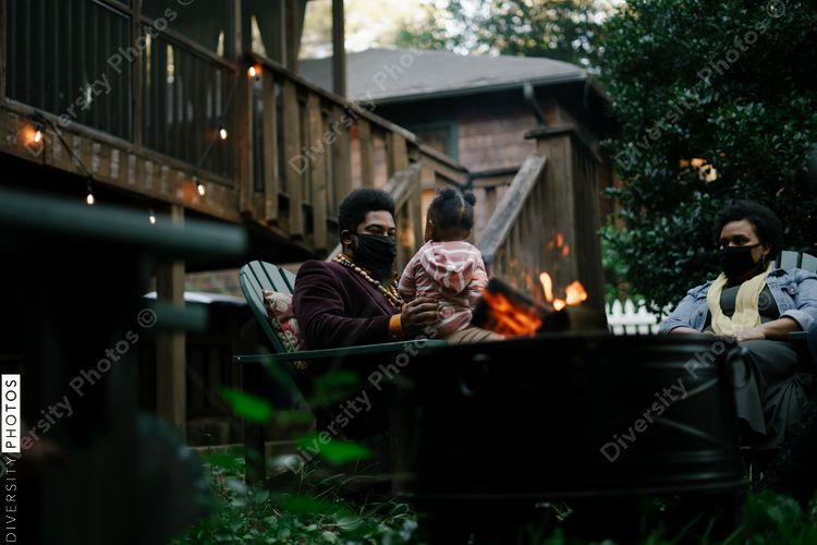 Black friends sitting around firepit safely wearing mask in backyard