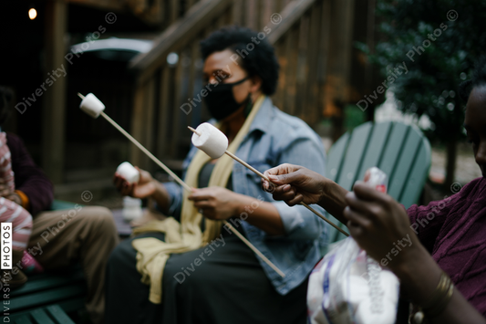 Black friends gathering around fire-pit roasting marshmallows and eating smores