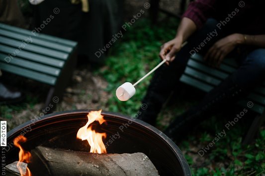 Black friends gathering around fire-pit roasting marshmallows and eating smores