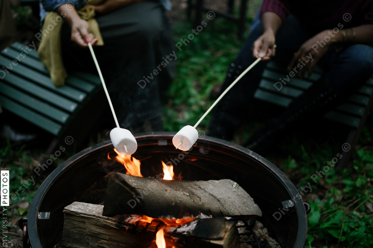 Black friends gathering around fire-pit roasting marshmallows and eating smores