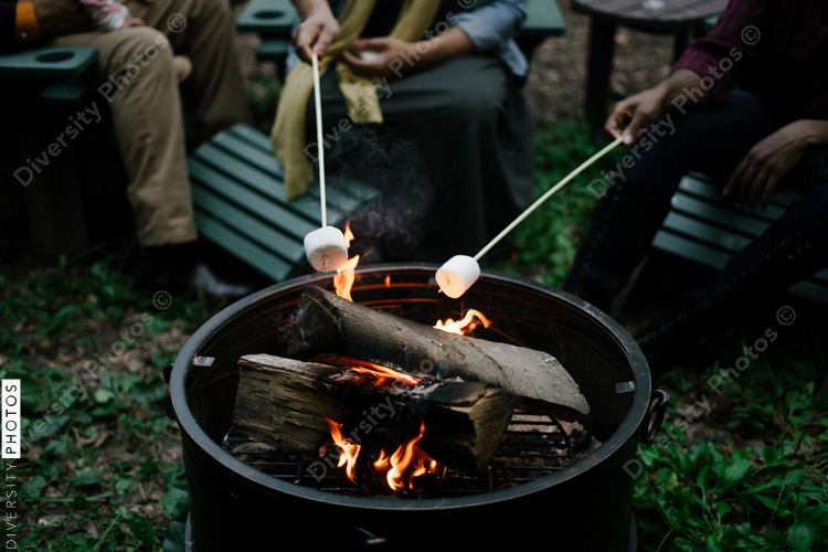 Black friends gathering around fire-pit roasting marshmallows and eating smores