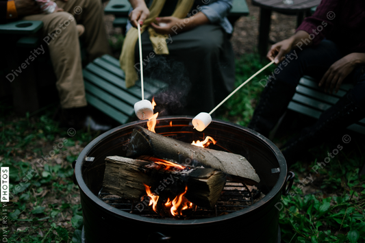 Black friends gathering around fire-pit roasting marshmallows and eating smores