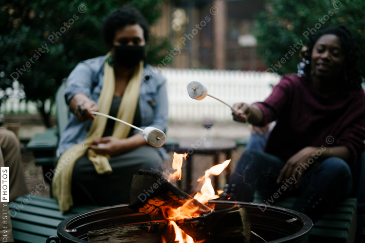 Black friends gathering around fire-pit roasting marshmallows and eating smores