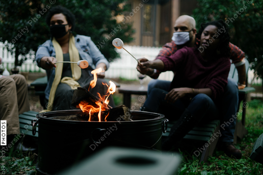 Black friends gathering around fire-pit roasting marshmallows and eating smores