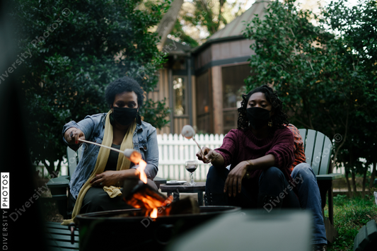 Black friends gathering around fire-pit roasting marshmallows and eating smores